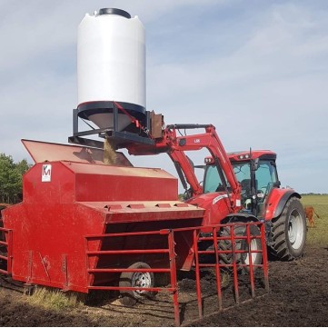 a red tractor emptying a 52 bushel pallet grain bin into a creep feeder