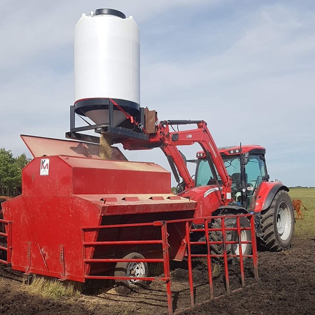 a red tractor emptying feed into a 52 bushel pallet grain bin into a creep feeder